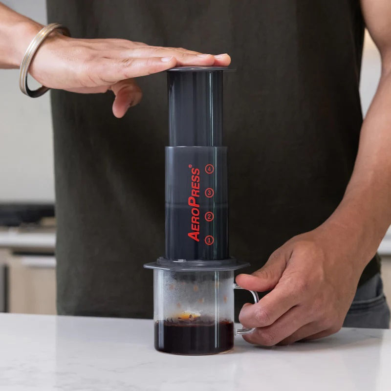 Comandante AeroPress filter paper pack with 350 sheets for coffee brewing, shown next to a coffee grinder.